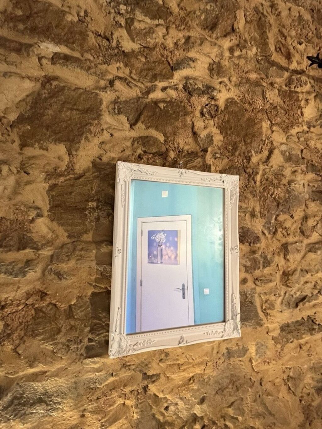 A framed picture of a door with a blue door and a white door, set against a textured stone wall.