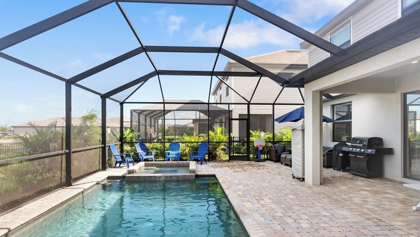 Zona de piscina exterior con sillas azules y una parrilla.