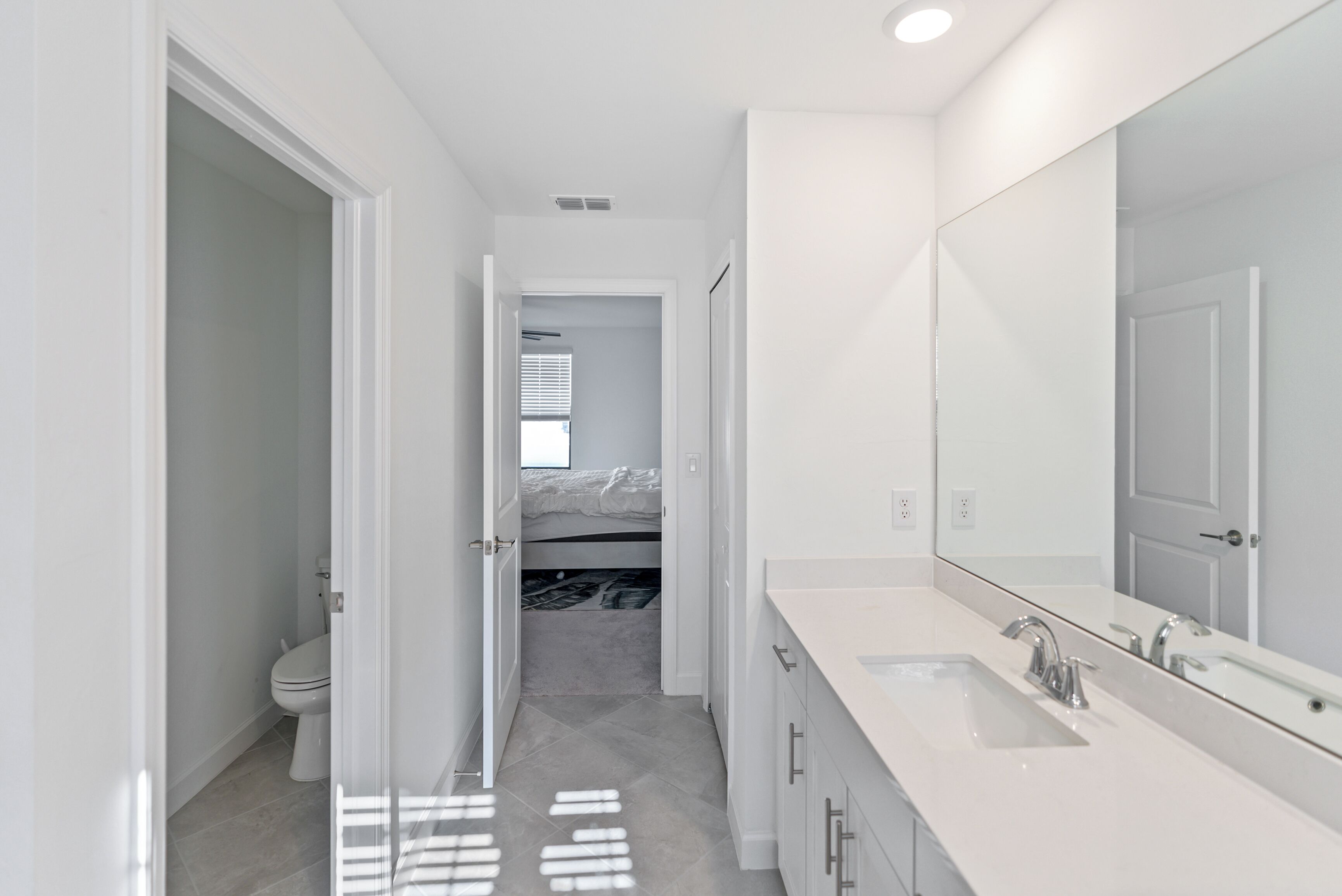 A modern bathroom with a large mirror, a white sink, and a toilet.