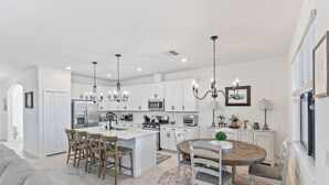 Una cocina moderna con armarios blancos, una isla central y un comedor con una mesa redonda y sillas.