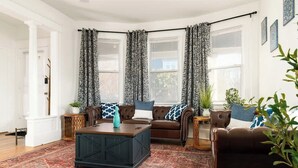 A living room with a brown leather sofa, a dark wooden coffee table, patterned curtains, and a red patterned rug. - Near NYC & Transit ~ Family Friendly ~ Whole House (New Rochelle)