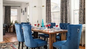 A dining area with a wooden table, blue upholstered chairs, and patterned curtains. - Near NYC & Transit ~ Family Friendly ~ Whole House (New Rochelle)