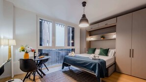 Une chambre moderne comprenant un lit, des tables de chevet, un bureau avec une chaise, une fenêtre et un balcon.