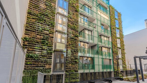 Un bâtiment moderne doté de jardins verticaux sur sa façade, de grandes fenêtres et de balcons avec des garde-corps verts.