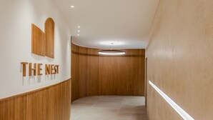 Un couloir aux murs lambrissés, sur lequel est accrochée une enseigne portant l’inscription « THE NEST ».
