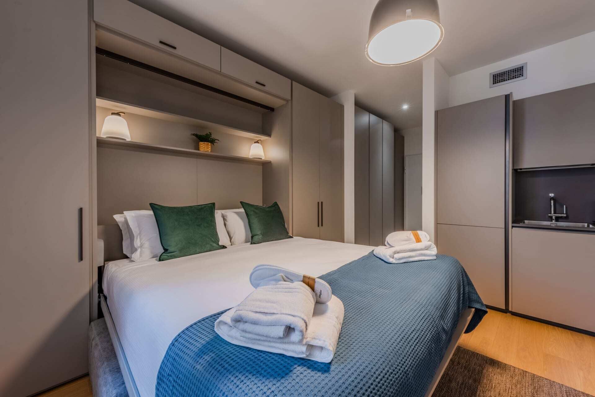 Una habitación de hotel moderna con una cama grande, armario empotrado y una pequeña kitchenette.