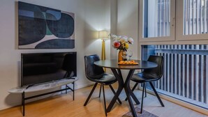 Un salon moderne avec un téléviseur à écran plat, deux fauteuils noirs, une table ronde ornée d’un vase de fleurs et un lampadaire.