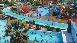 A water park with multiple slides and pools, surrounded by palm trees and shaded areas.