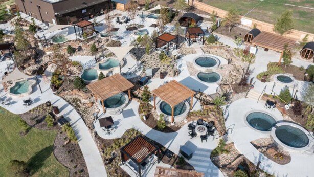 An aerial view of a resort with multiple swimming pools, outdoor seating areas, and a large building in the background.