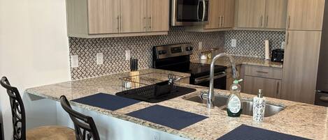 A modern kitchen with wooden cabinets, a stainless steel microwave, and a granite countertop.