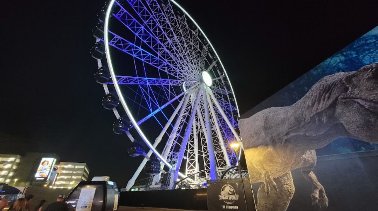 A large Ferris wheel with a dinosaur statue beside it.