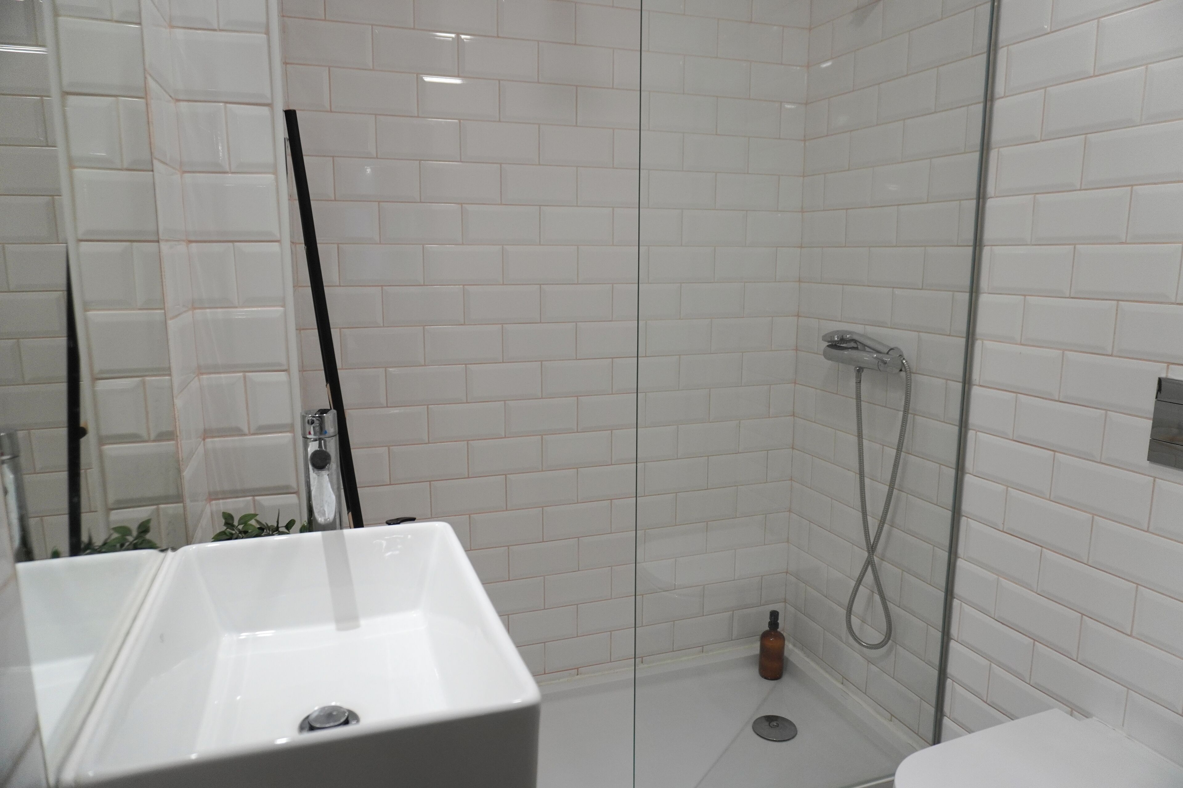 Une salle de bain moderne avec des carreaux de métro blancs, une douche en verre, un lavabo blanc et des toilettes.