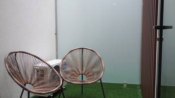 Two wicker chairs with metal legs, a white table, and a glass partition in a room with artificial green flooring.