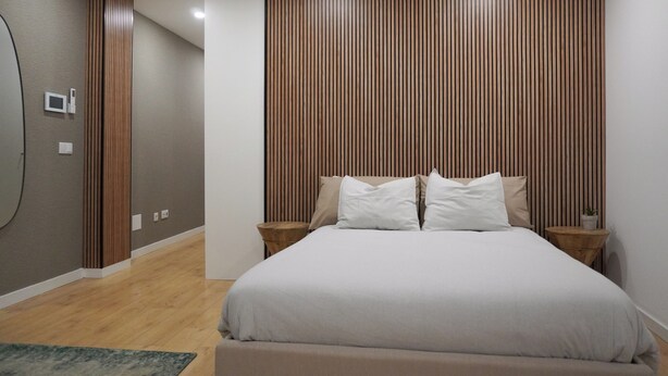 A modern bedroom with a large bed, wooden panel wall, two bedside tables, and a small potted plant. - In the heart of Aveiro! Cozy accommodation in Portuguese Venice (Aveiro)