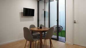 A modern dining area with a round wooden table, four chairs, a small potted plant, and a flat-screen TV mounted on the wall. - In the heart of Aveiro! Cozy accommodation in Portuguese Venice (Aveiro)