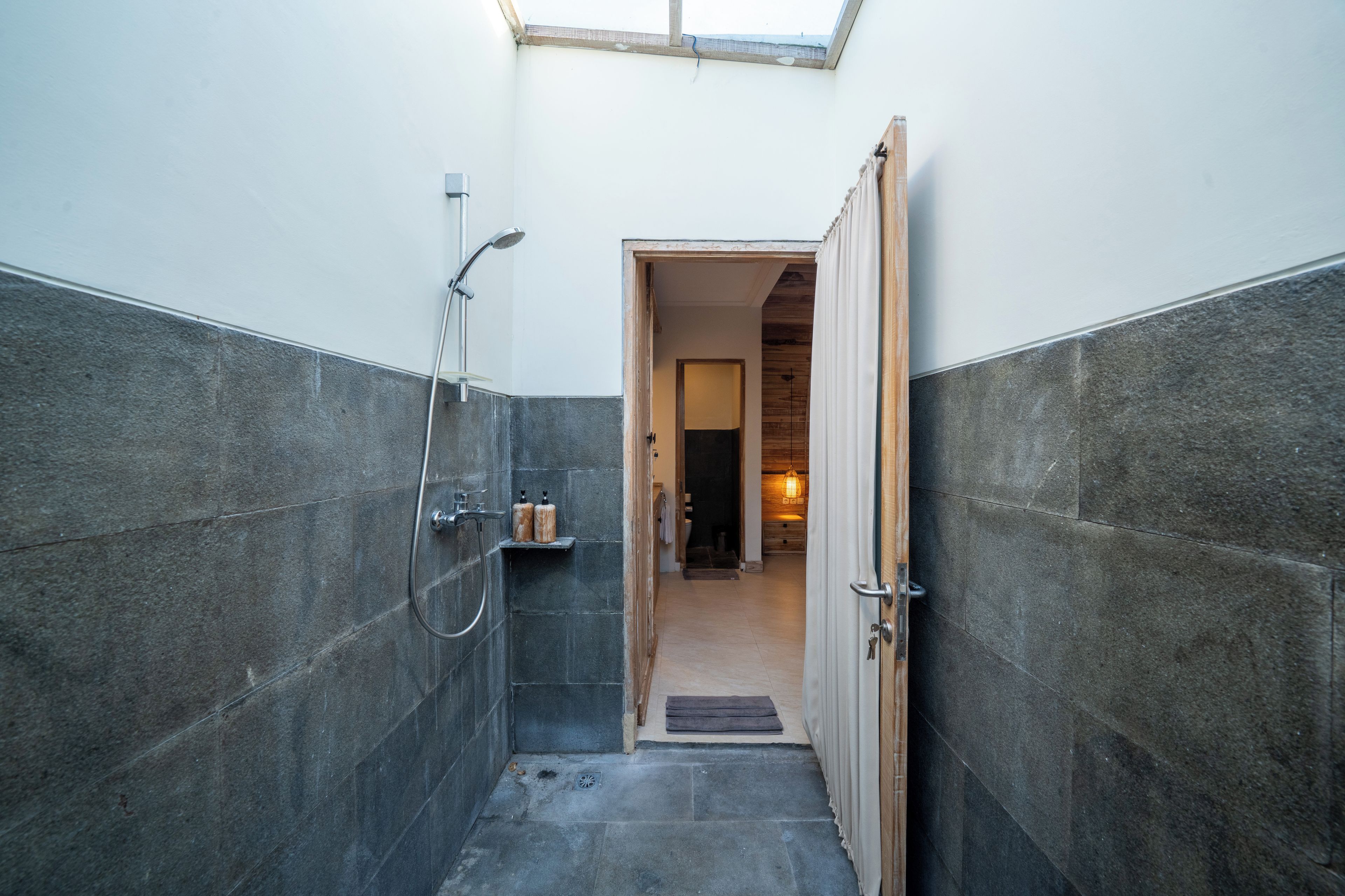 Een badkamer met een douche, een klein plankje met toiletartikelen en een houten deur naar een andere kamer.