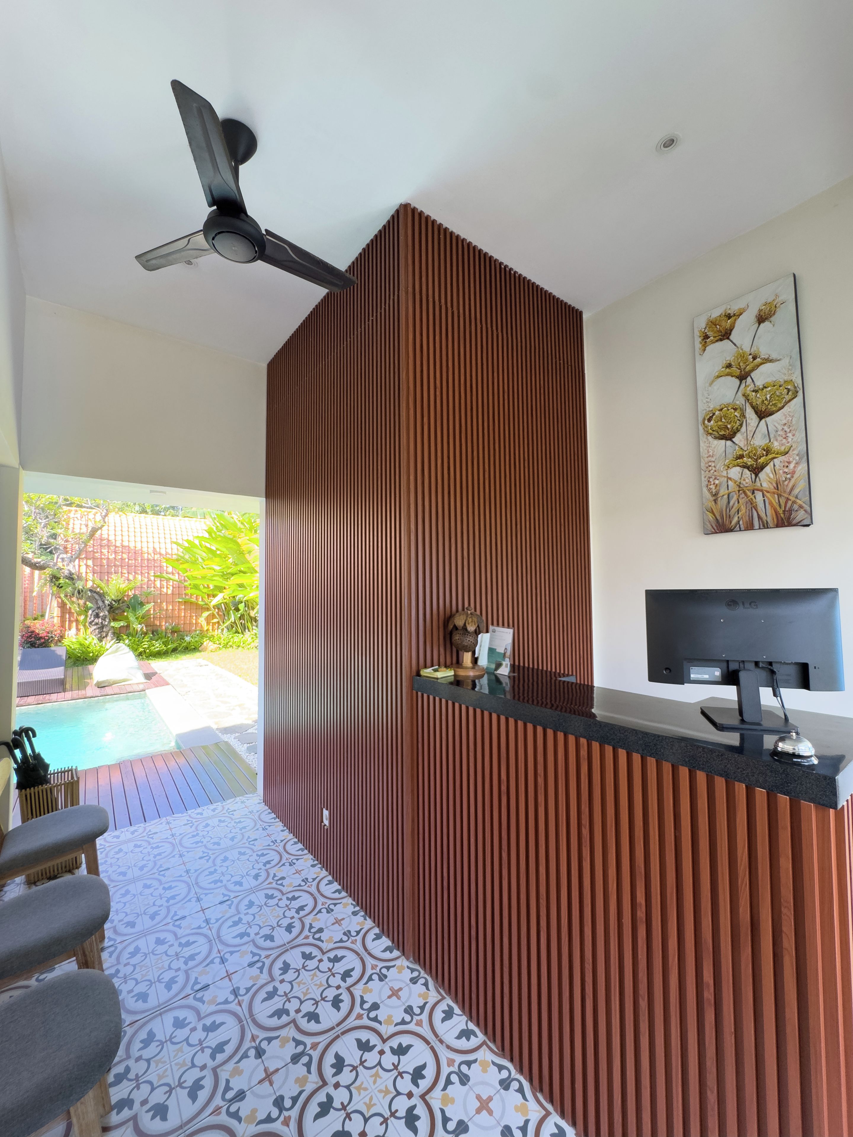 Ein Empfangsbereich mit einer Wandpaneele aus Holz, einem Deckenventilator, einem Flachbildfernseher und Blick auf einen Swimmingpool.