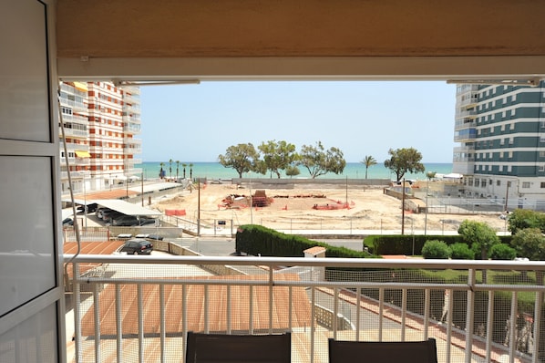 Une vue depuis un balcon donnant sur une plage, avec des constructions, des arbres et des bâtiments en arrière-plan.