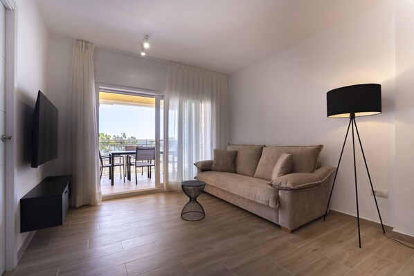 A living room with a sofa, a TV, a floor lamp, and a view of an outdoor balcony. - ESTORIL BLOCK 3 PREMIUM (Benicàssim)