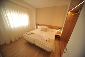 Une chambre d’hôtel avec un grand lit, une tête de lit en bois, une table de chevet avec une lampe et une armoire.