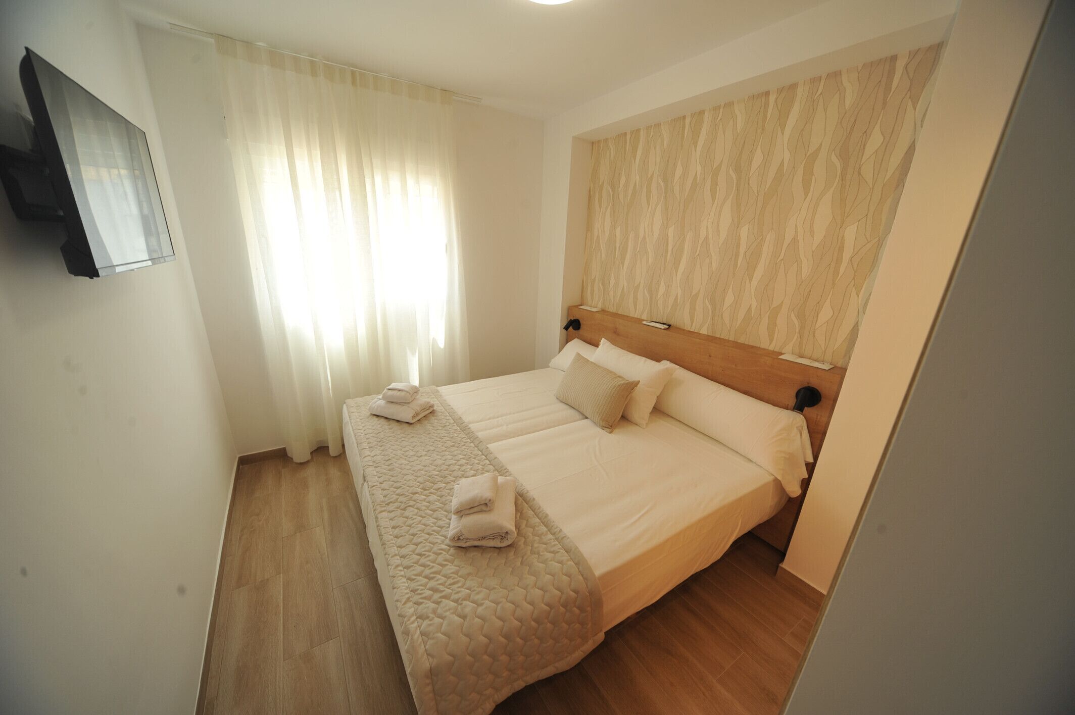 A hotel room with a bed, two pillows, a blanket, and a TV mounted on the wall.