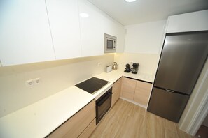 A modern kitchen with a built-in microwave, a stainless steel refrigerator, a black induction cooktop, and wooden cabinets. - ESTORIL BLOCK 3 PREMIUM (Benicàssim)