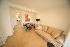 A modern living room with a sofa, a dining table with chairs, a floor lamp, and a painting on the wall.