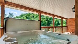 A hot tub with a wooden deck and a view of a forest. - Tranquil Haven - Modern Cabin Retreat - Book Your Spring Break Now (Sevierville)
