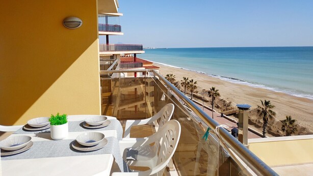 A balcony with a table set for dining, overlooking a beach with palm trees and a clear blue sky. - MOLI DE VENT SUPERIOR (Peñiscola)