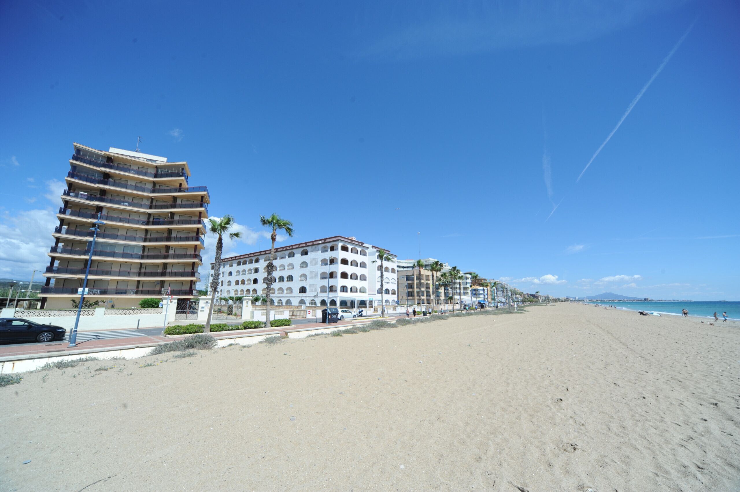 A beachfront hotel with multiple floors, a sandy beach in the foreground, and a clear blue sky.