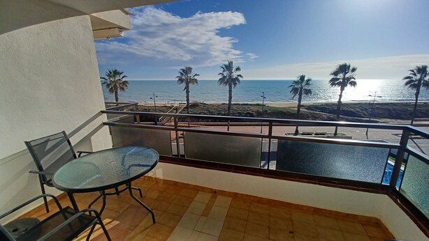A balcony with a glass table and chairs, overlooking a beach with palm trees and the ocean. - EL PARAISO OCEAN VIEW (Peñiscola)