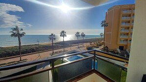 A balcony with a pool, overlooking a beach with palm trees and a building with balconies. - EL PARAISO OCEAN VIEW (Peñiscola)
