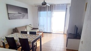A spacious living area with a dining table, chairs, a sofa, a ceiling fan, and a large window with curtains. - EL PARAISO OCEAN VIEW (Peñiscola)