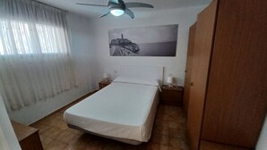 A bedroom with a bed, a ceiling fan, a nightstand with a lamp, a wardrobe, and a framed picture on the wall. - EL PARAISO OCEAN VIEW (Peñiscola)