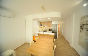 A modern kitchen with a central island, white walls, and a wooden dining table. - PRINCICASIM (Benicàssim)