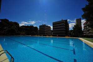 A swimming pool with clear blue water, surrounded by buildings and trees. - PRINCICASIM PREMIUM (Benicàssim)