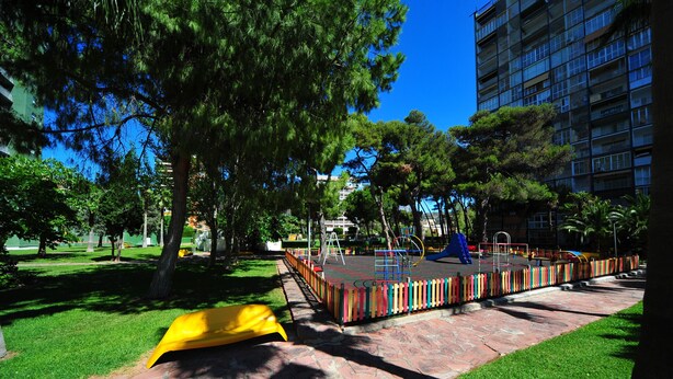 Un parque infantil con valla de colores, un tobogán amarillo y una estructura azul para escalar.