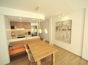 Eine moderne Küche mit integrierten Geräten, ein Essbereich mit Holztisch und -stühlen sowie ein großes abstraktes Gemälde an der Wand.