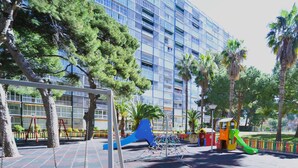 A playground with swings and slides, surrounded by trees and a building in the background. - PRINCICASIM (Benicàssim)