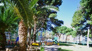 A paved pathway in a park with palm trees and a playground. - PRINCICASIM (Benicàssim)