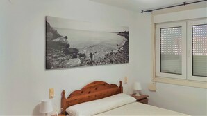 Een slaapkamer met een bed, nachtkastje, wandlamp, plafondventilator en een raam met jaloezieën.