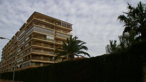 Een meerlaags woongebouw met balkons, een bakstenen muur en een palmboom.