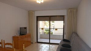 A living room with a sofa, a wooden cabinet, a television, and a balcony with a view of the outside. - UPPER SHORE (Alcoceber / Alcossebre)