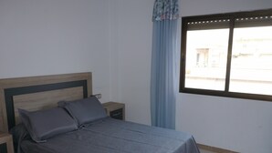 A bedroom with a bed, nightstands, a window with curtains, and a view of buildings outside. - UPPER SHORE (Alcoceber / Alcossebre)