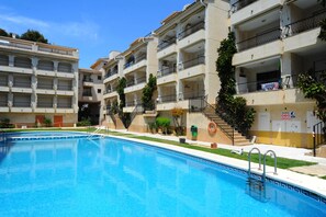 A swimming pool with a clear blue water, surrounded by multi-story buildings with balconies and a staircase leading to the upper floors.
