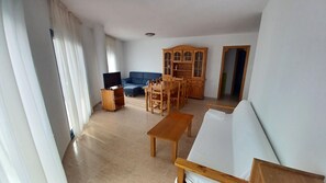 A living room with a blue sofa, wooden dining table, and a TV stand. - TWO BAYS SEA VIEW (Peñiscola)