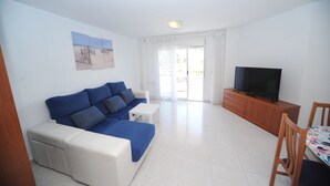Una sala de estar con un sofá azul, una mesa de centro blanca y un televisor sobre un mueble de madera.