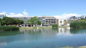 Un entorno tranquilo junto al lago con edificios modernos al fondo, cielo despejado y superficie acuática en calma.
