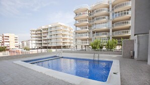 A swimming pool area with a pool, surrounded by a low stone wall, and adjacent to a multi-story residential building with balconies. - BAIX MAESTRAT (Peñiscola)