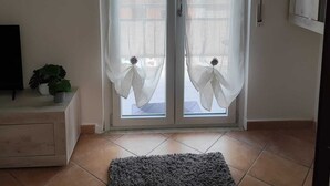 A room with a sliding glass door, a small white cabinet, a potted plant, and a grey rug on the floor. - Palmi Bay Home (Palmi)